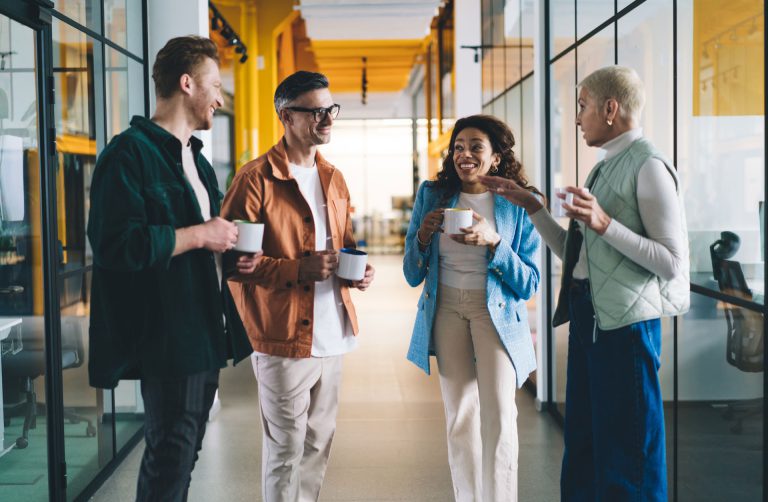 Four colleagues chatting over coffee in a glass-walled office